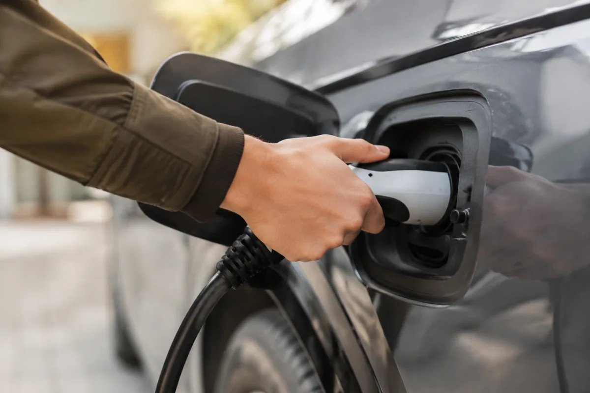 Aide pour l'achat d'une voiture électrique : ce que vous pouvez vraiment cumuler Main branchant un câble de recharge sur la prise d'une voiture électrique blanche