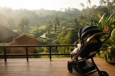 Famille se promenant sur une plage de sable noir à Bali sous un ciel nuageux, poussette et sac à langer visibles